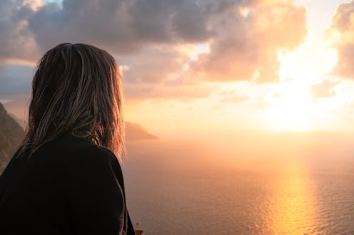 A girl with her back turned is gazing at the stunning sunset over the sea in Mallorca. The scene cap...
