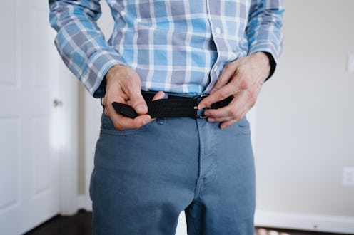 Close-up of unrecognizable white man putting on his belt while dressing