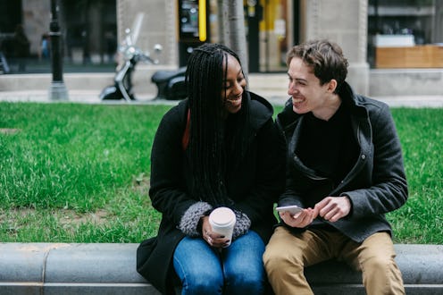 Two friends sharing a lighthearted moment as they look at a smartphone while enjoying coffee, dresse...