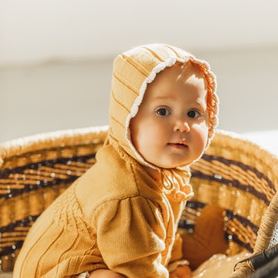 Adorable beautiful six month old baby girl sitting in vintage baby wicker cot. Little infant waking up in moses basket at the light morning. Concept of natural organic baby clothes and eco bedding set.