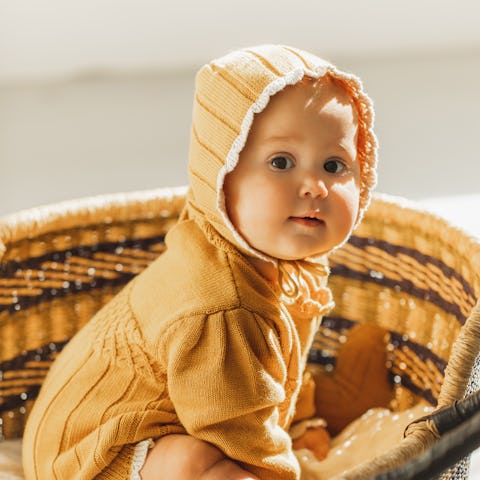 Adorable beautiful six month old baby girl sitting in vintage baby wicker cot. Little infant waking ...