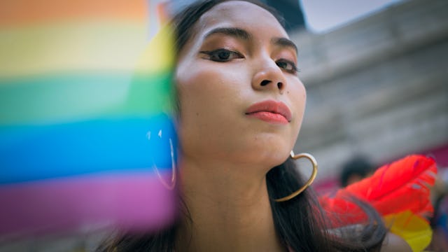 A close-up portrait of a young woman with long hair, wearing large hoop earrings, confidently holdin...