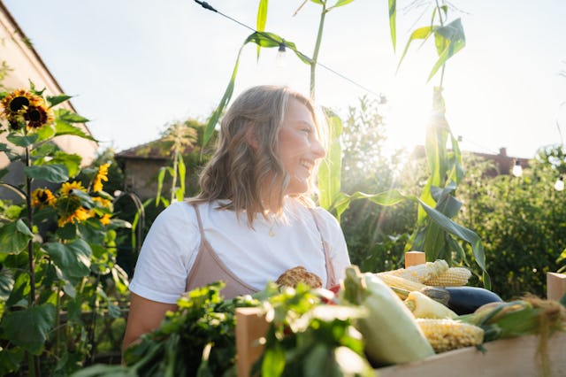 Photo of a smiling woman holding a crate in her hands, full of fresh, home-grown vegetables