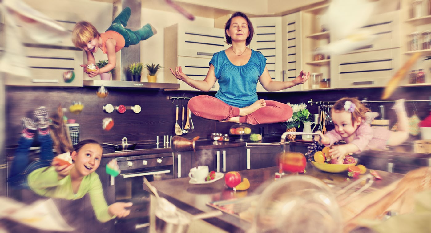 Mother meditating at the kitchen with her children flying around