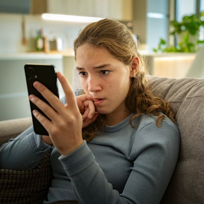 Portrait of a nervous teen girl looking at her smartphone. Teenagers have become more likely to say social media is bad for them since 2022.