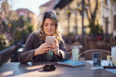 Smiling woman reading a text message on cell phone while spending a day in a café.
