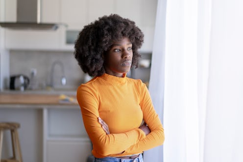 Sad afro-american woman looking through window with hands crossed
