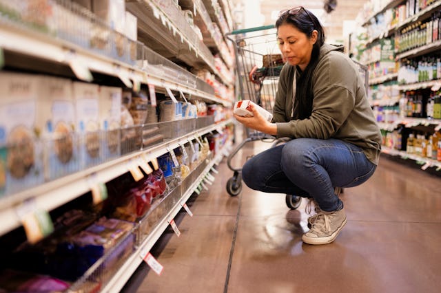 A woman reads the back of boxed pasta on the lower shelf in the grocery store aisle.