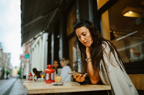 Tourist or a local woman sitting in a cafe in Amsterdam. She is checking mobile apps, going through ...