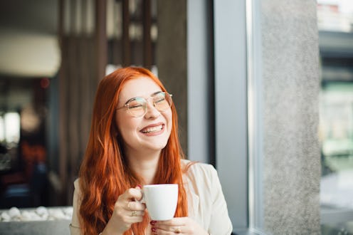 Portrait of a redhead smiling young elegant woman, sitting by the window in a restaurant, smiling an...