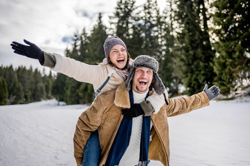 Young couple having fun on winter vacation, boyfriend piggybacking girlfriend while enjoying time to...