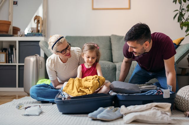 Happy daughter having fun while helping her parents to pack luggage in a living room.