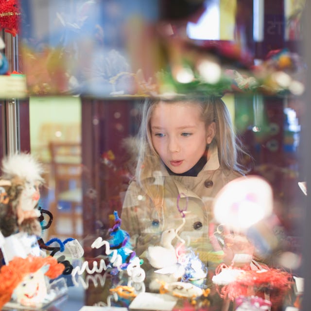 A young girl gazes in awe at colorful, handmade figurines displayed behind glass, her expression fil...