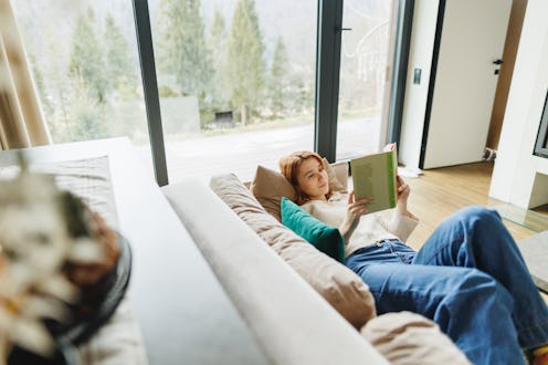 A young woman lies comfortably on a plush sofa, fully engrossed in her book