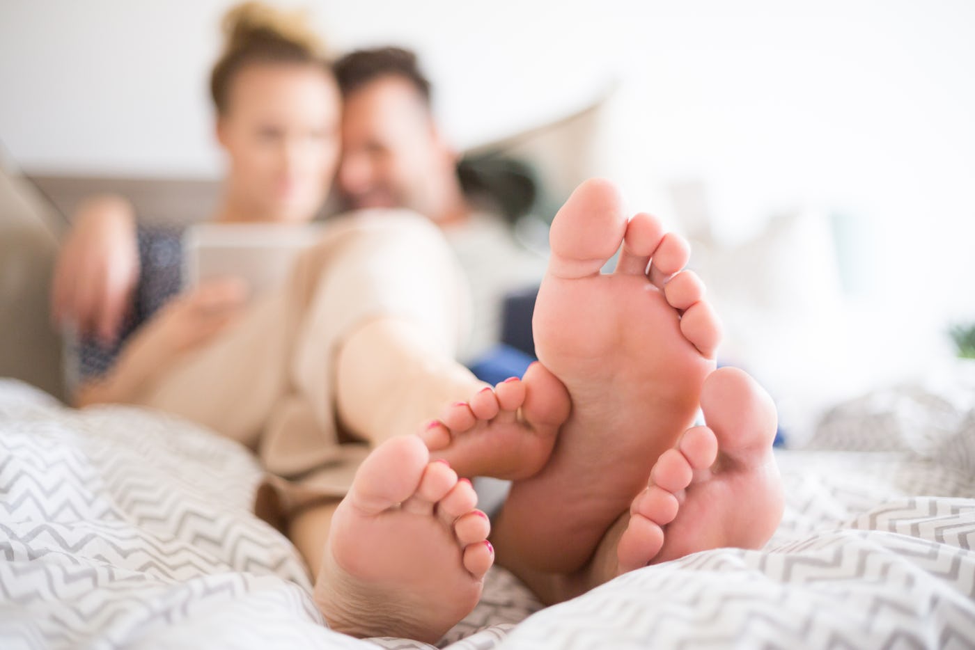 Couple lying on the bed in the bedroom in the morning and using digital tablet. Focus on feet.