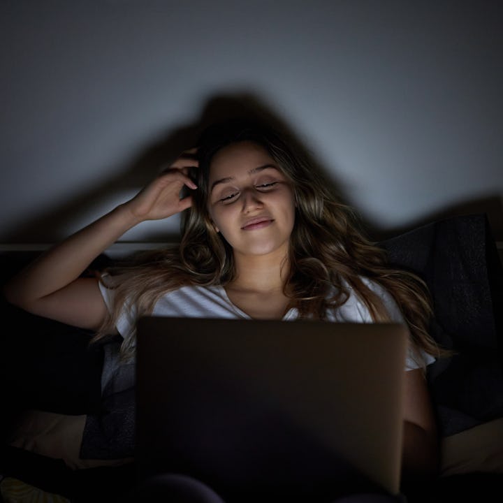 Happy and cheerful woman with laptop in her bedroom bed.