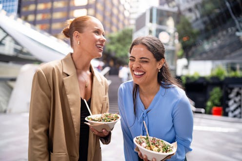 Cheerful women sharing a moment of joy while enjoying healthy meals in a bustling urban outdoor sett...