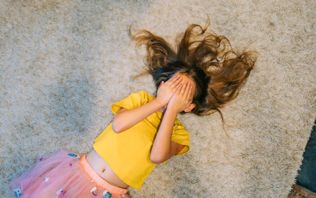 Young girl lies on the floor and covers her face with her hands