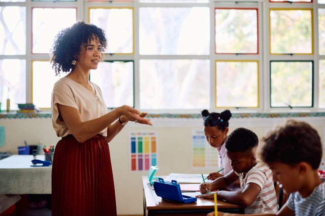 Female teacher in her 20s talking to class, gesturing with hands