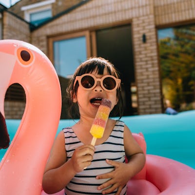 Cute Asian toddler cooling down with ice lolly while enjoying summer in the backyard. Summer vacation.