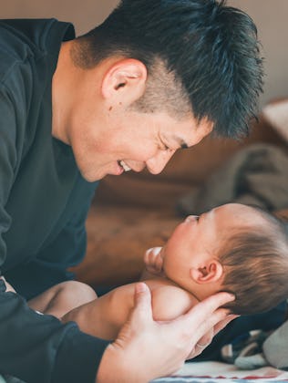A joyful moment between a father and his baby, both smiling while sitting on the floor.