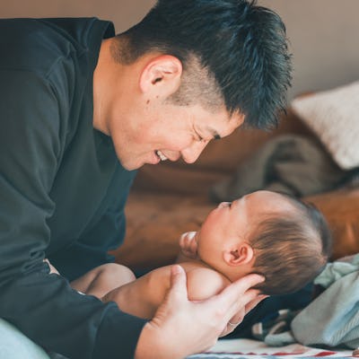 A joyful moment between a father and his baby, both smiling while sitting on the floor.
