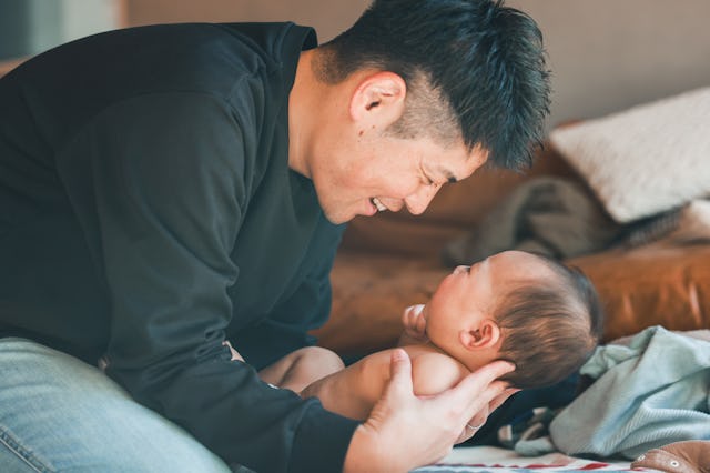 A joyful moment between a father and his baby, both smiling while sitting on the floor.