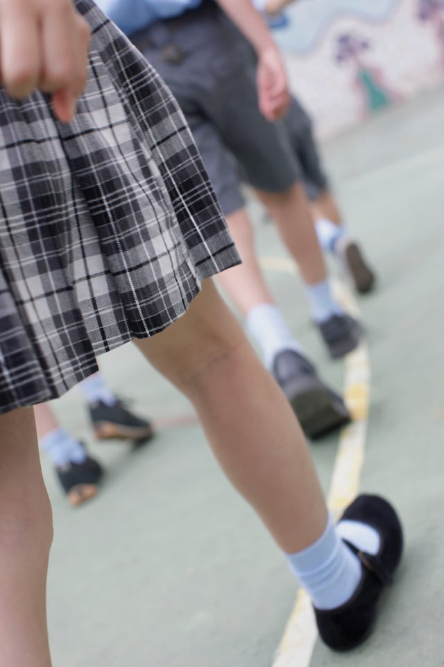 A close-up view of children walking on a playground. Focus on a girl's plaid skirt and legs, with ot...