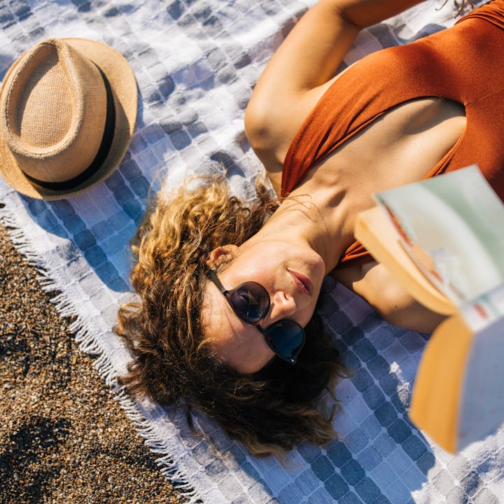 Woman lies on the beach reading a book