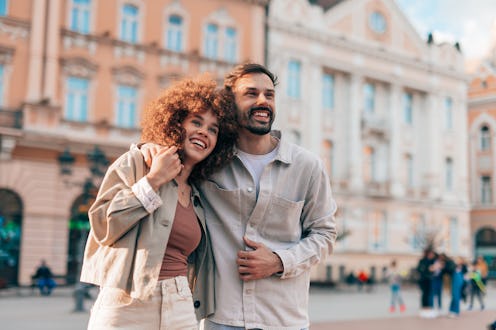 Young couple enjoying a sunny day in the city, embracing and smiling while exploring the vibrant str...