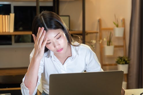 Exhausted woman sitting at her desk in a home office, holding her head in frustration while working ...