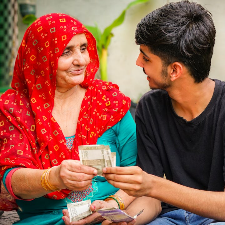 Portrait of traditional indian senior woman giving money to her teenage grandson. She is wearing tra...
