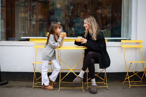 Young kid girl smiling. She sitting in cozy cafe with light interior and spending time with happy mu...