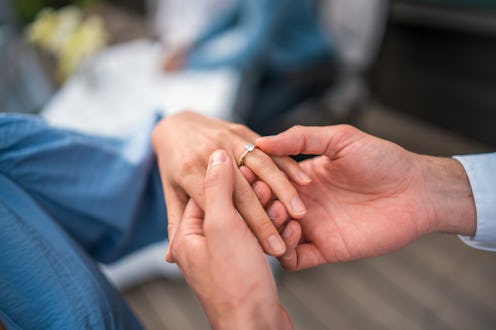 Mid adult Latin man slips engagement ring on Caucasian woman's finger. They sit together, joy eviden...