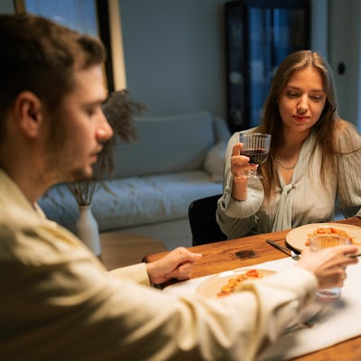 A man and a woman drink wine from glasses sitting at a table during a romantic dinner at home