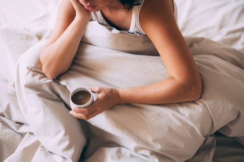 A woman comfortably rests in bed, sipping a warm cup of coffee. The serene morning ambiance emphasiz...