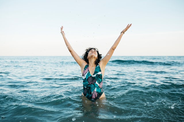 Young latin woman wearing swimsuit in the sea splashing water to the air