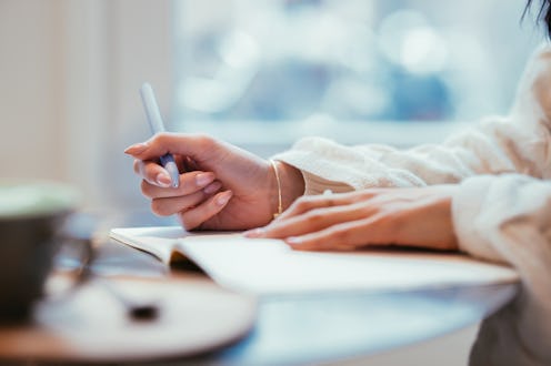 Close-up of a woman writing in a notebook with natural lighting, emphasizing creativity and thoughtf...