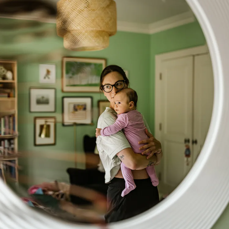 Young mother with baby at home. Young mother dressed in casual clothes wearing glasses, holding 3 mo...