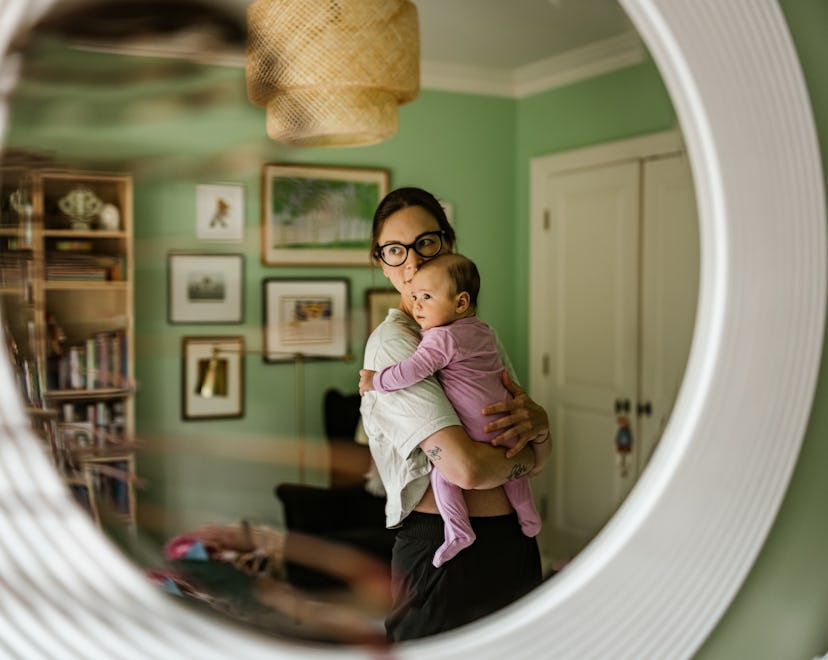 Young mother with baby at home. Young mother dressed in casual clothes wearing glasses, holding 3 mo...