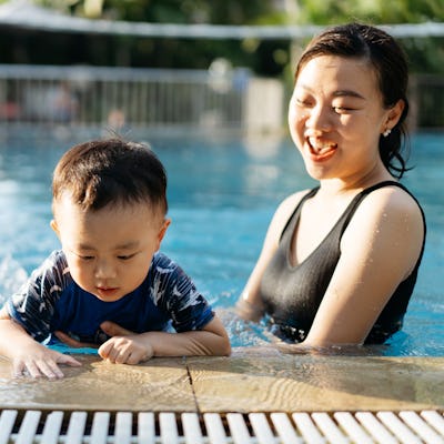 A mother and child taking a dip in the pool on a hot summer day. They are both laughing and having fun.