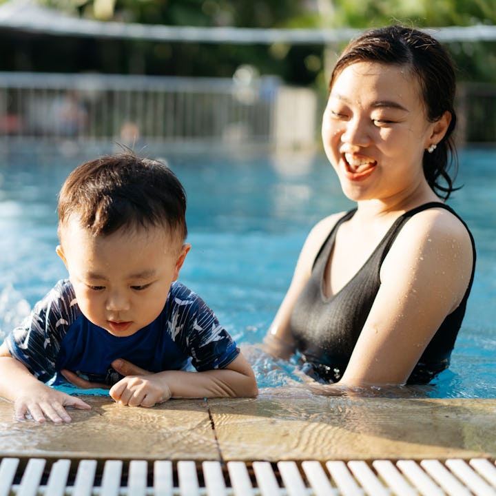 A mother and child taking a dip in the pool on a hot summer day. They are both laughing and having f...