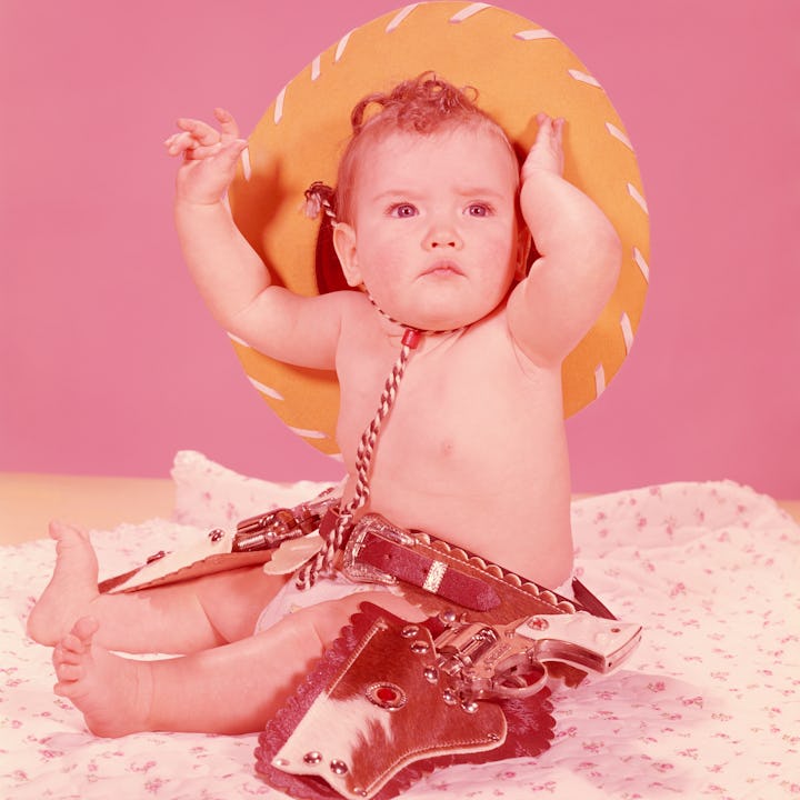 UNITED STATES - CIRCA 1950s: Baby wearing cowboy hat and holster, dressed as a cowgirl, portrait.