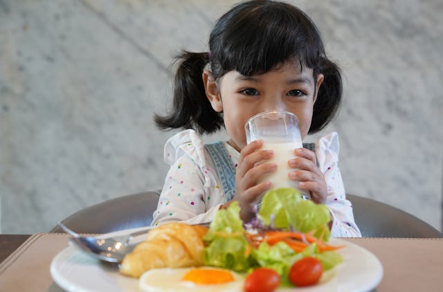 A little girl is drinking a glass of milk and enjoy eating a healthy breakfast.