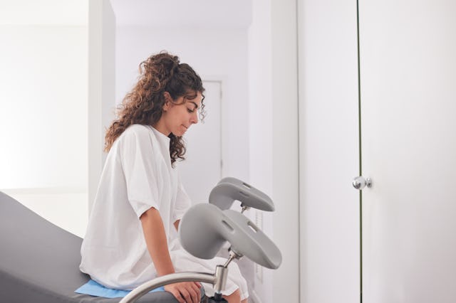 A young patient in hospital gown, awaiting the gynecologist in the doctor’s office.