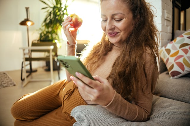 Pregnant woman sits at home and eats an apple