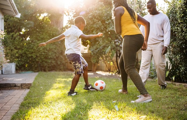 Small boy playing soccer with his sister and father in the backyard garden