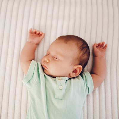 Sleeping baby, close up, arms raised over head on a beige sleep surface.