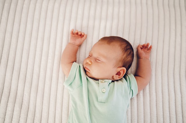Sleeping baby, close up, arms raised over head on a beige sleep surface.