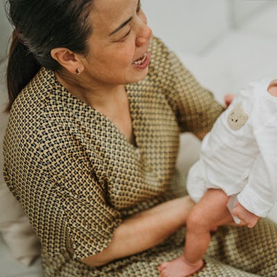 A woman in a patterned robe joyfully holds a newborn baby dressed in a white onesie.